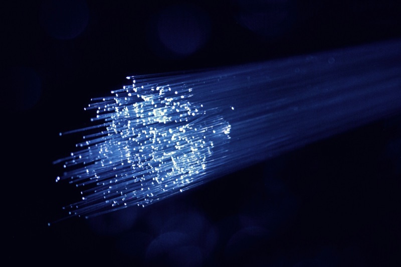 A bundle of optical fibres carrying blue light, their cut ends glowing against a dark background.