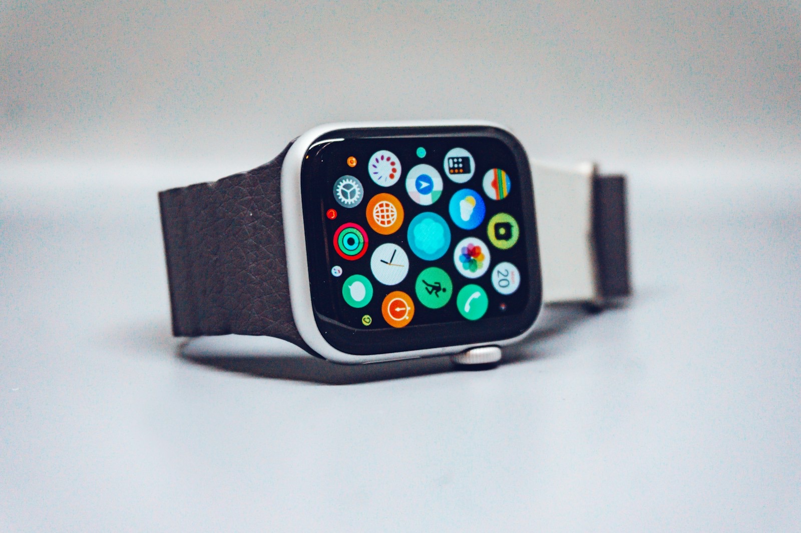 An Apple Watch lying on its side on a grey surface, its screen showing the grid of app icons, including Activity and Workout.