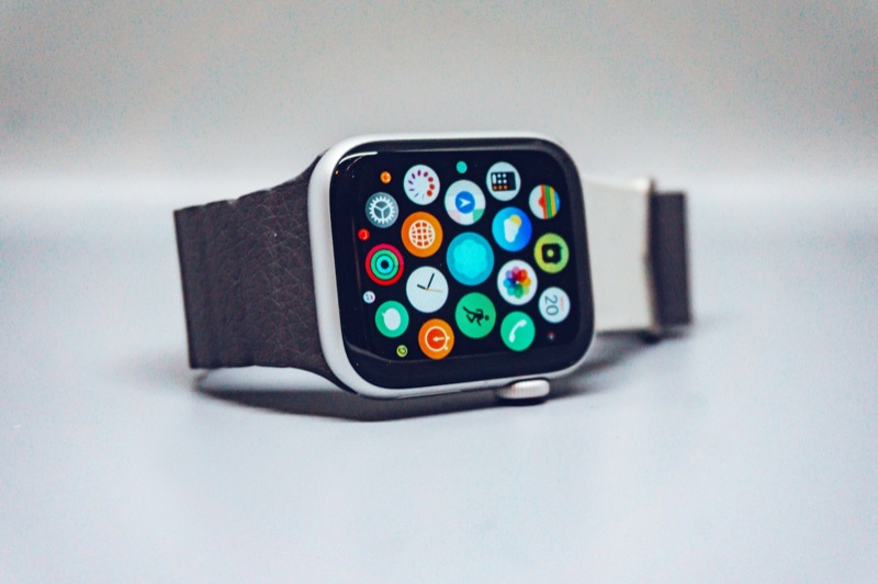 An Apple Watch lying on its side on a grey surface, its screen showing the grid of app icons, including Activity and Workout.
