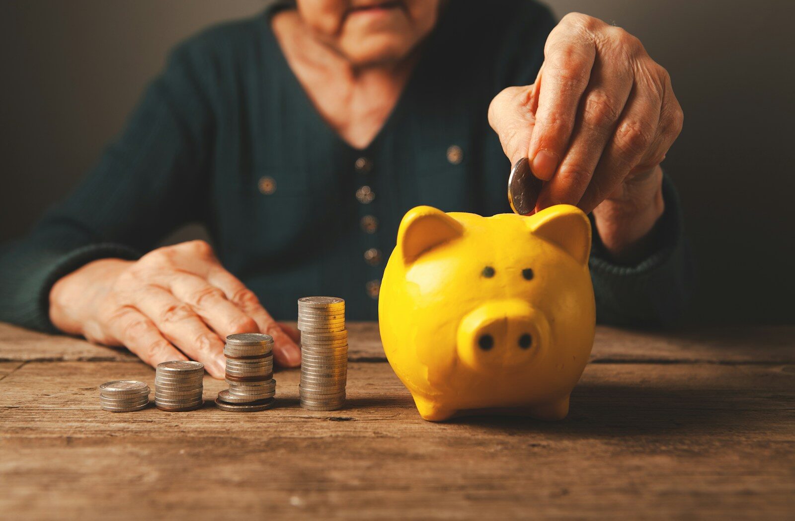 An older woman placing a coin into a piggy bank