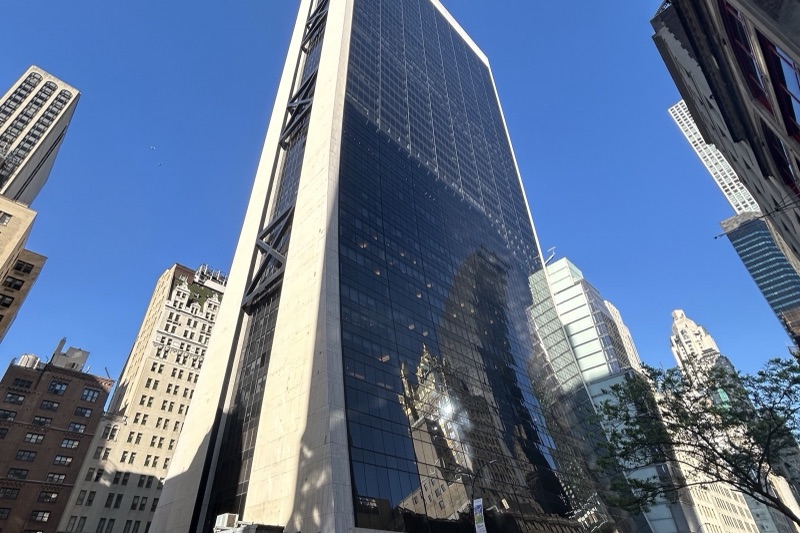 The black glass and white travertine Solow Building at 9 West 57th Street in Manhattan, seen from street level against a blue sky, with older towers on either side.