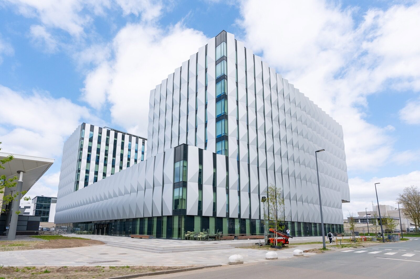 A large office building on ASML's campus in Veldhoven, the Netherlands, clad in angular white aluminium panels, under a partly cloudy sky.