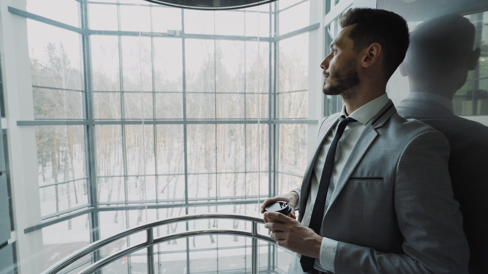 An executive in a suit standing at a large office window, looking out
