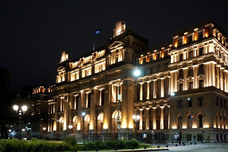 The Palacio de Justicia in Buenos Aires, lit at night, with its columned facade and Argentine flag above the central tower.