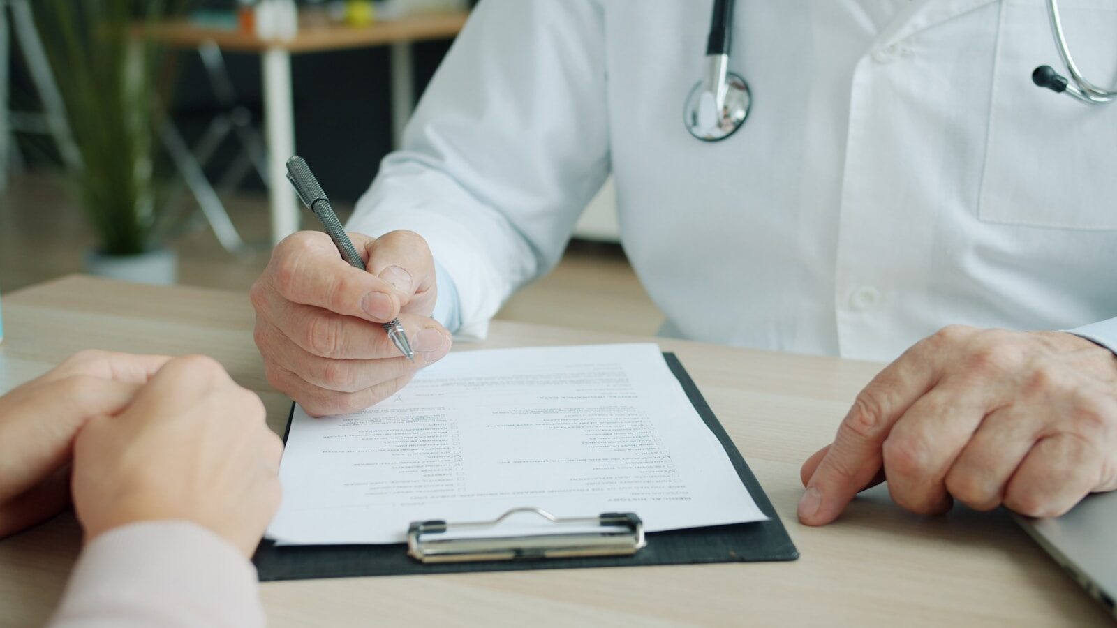 A physician writing on a patient's chart during a consultation