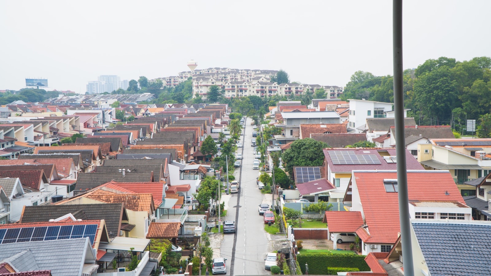 An elevated view shows a long, straight residential street lined with rows of multi-story houses featuring red and grey tiled roofs