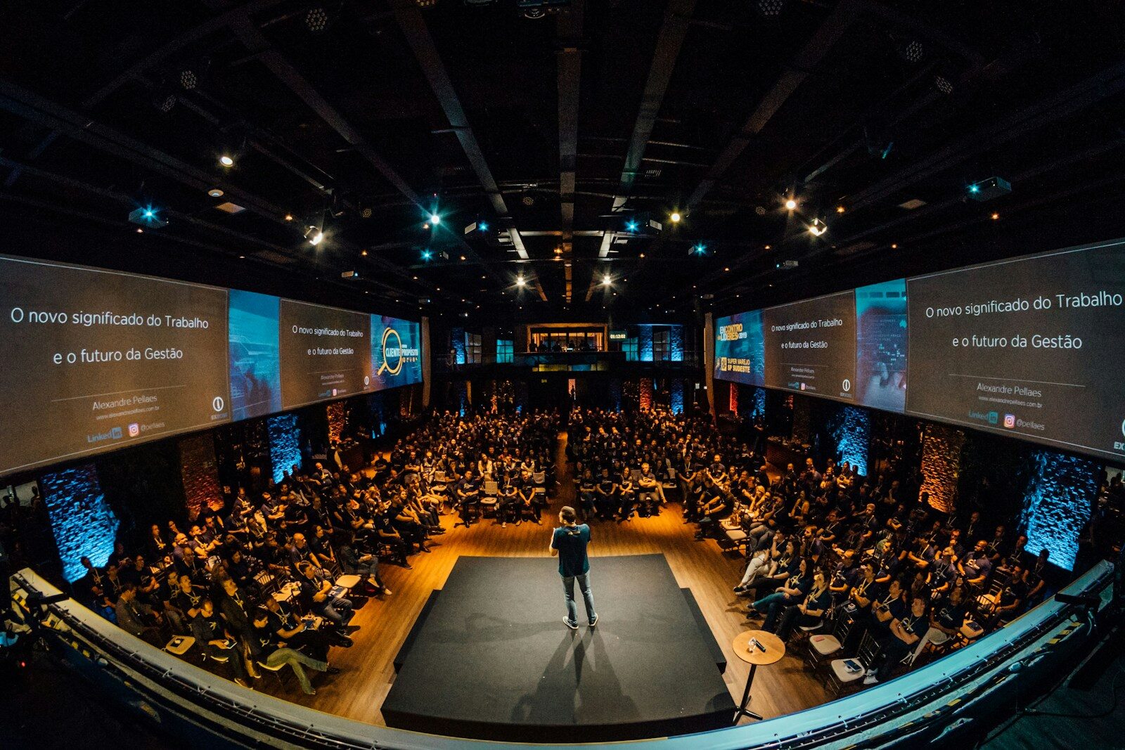 A speaker addressing a large seated conference audience from a stage