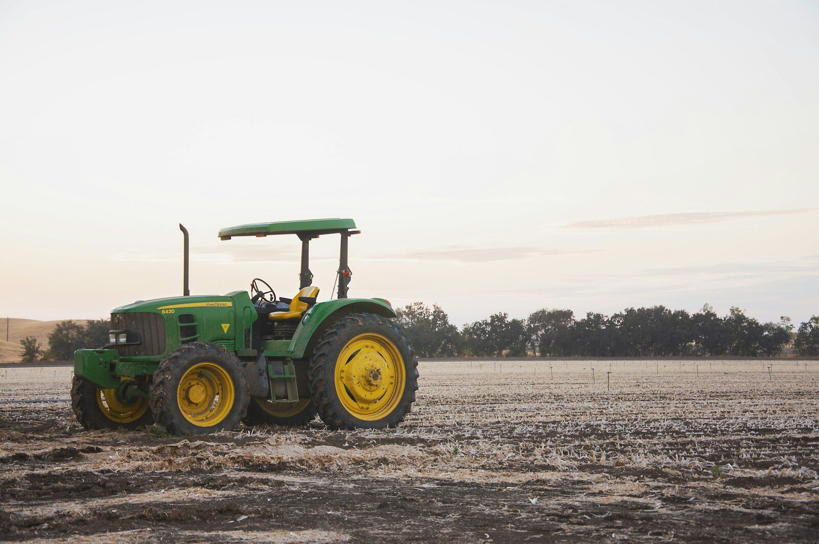 A green tractor standing in a field at sunset