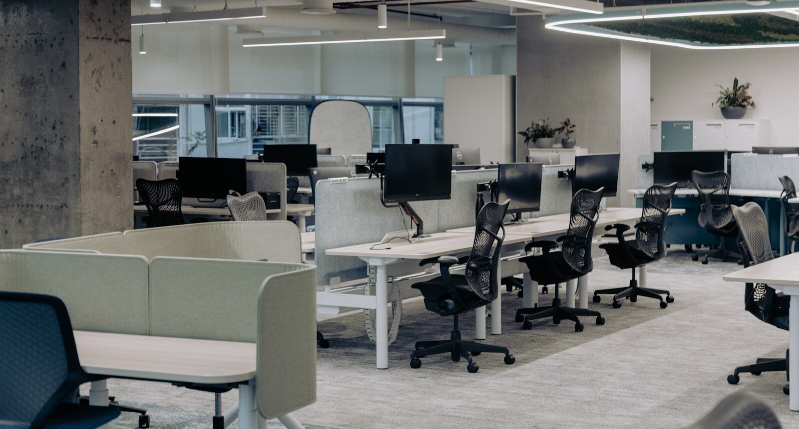 Rows of empty desks and chairs with dark monitors in an open-plan office.