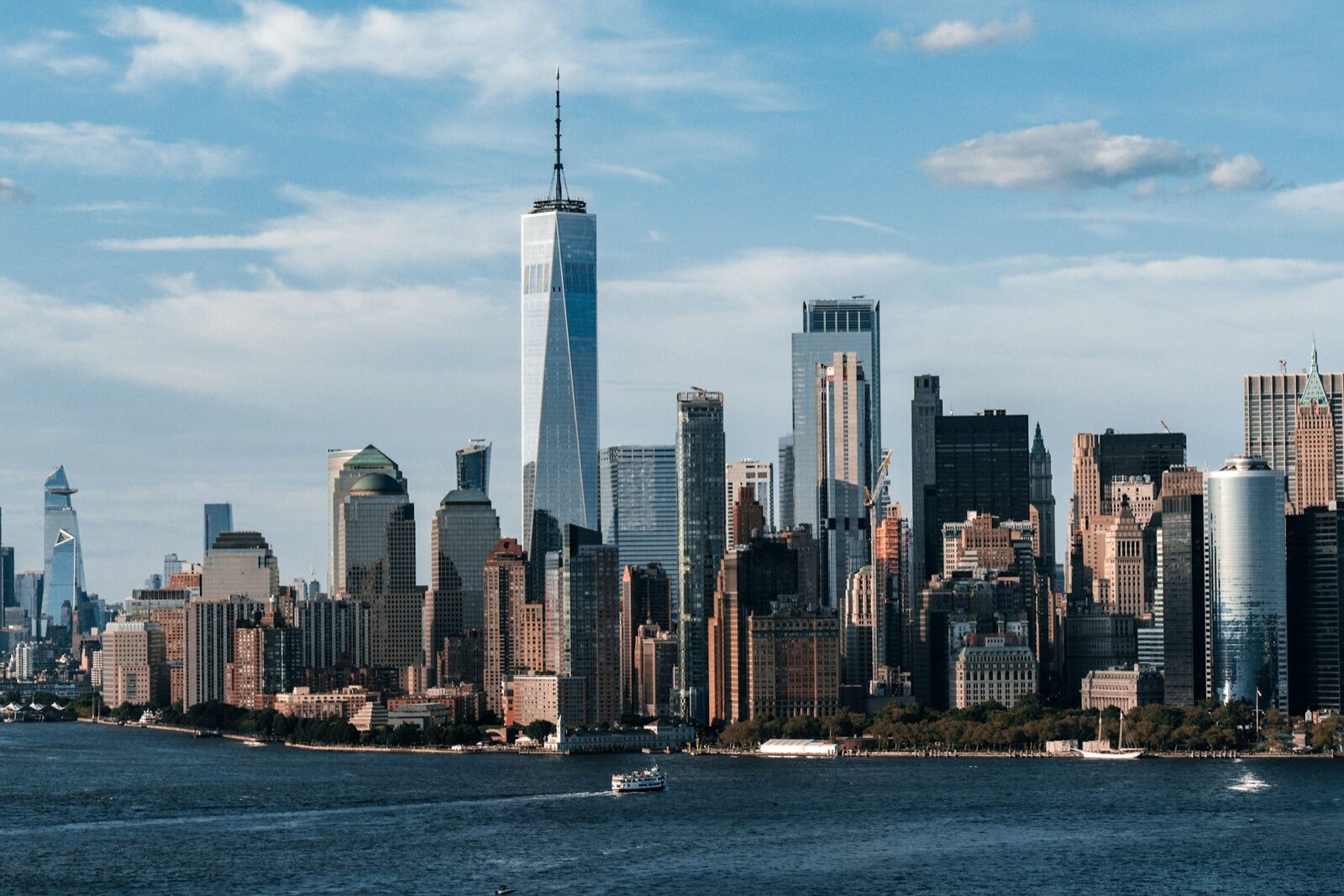 The Lower Manhattan skyline seen across the water under a blue sky.
