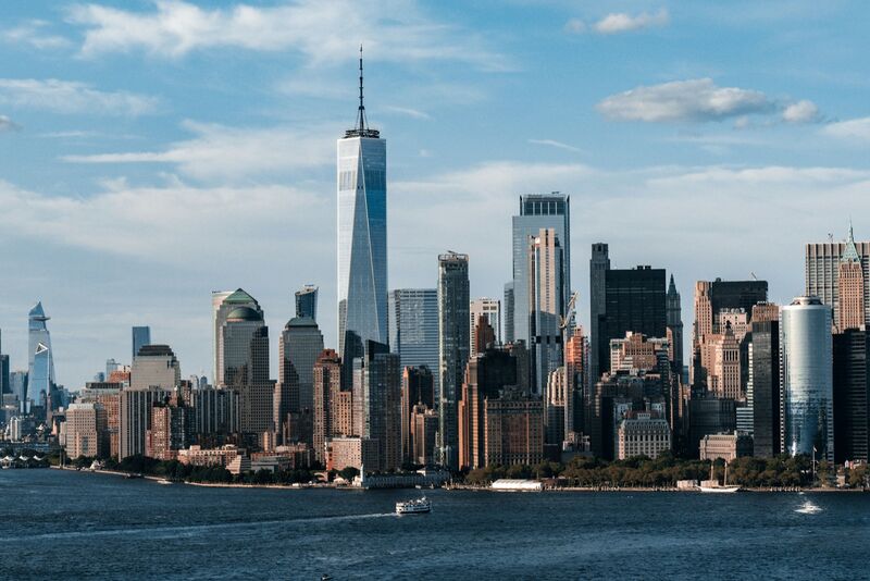 The Lower Manhattan skyline seen across the water under a blue sky.