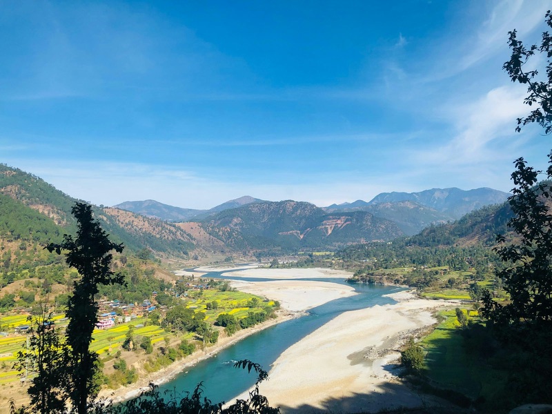 A braided river running through a steep Nepali valley, with terraced fields and a village on the slope above it.