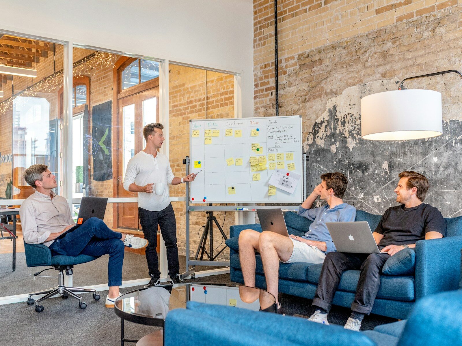 Three people working on laptops while a colleague presents at a whiteboard