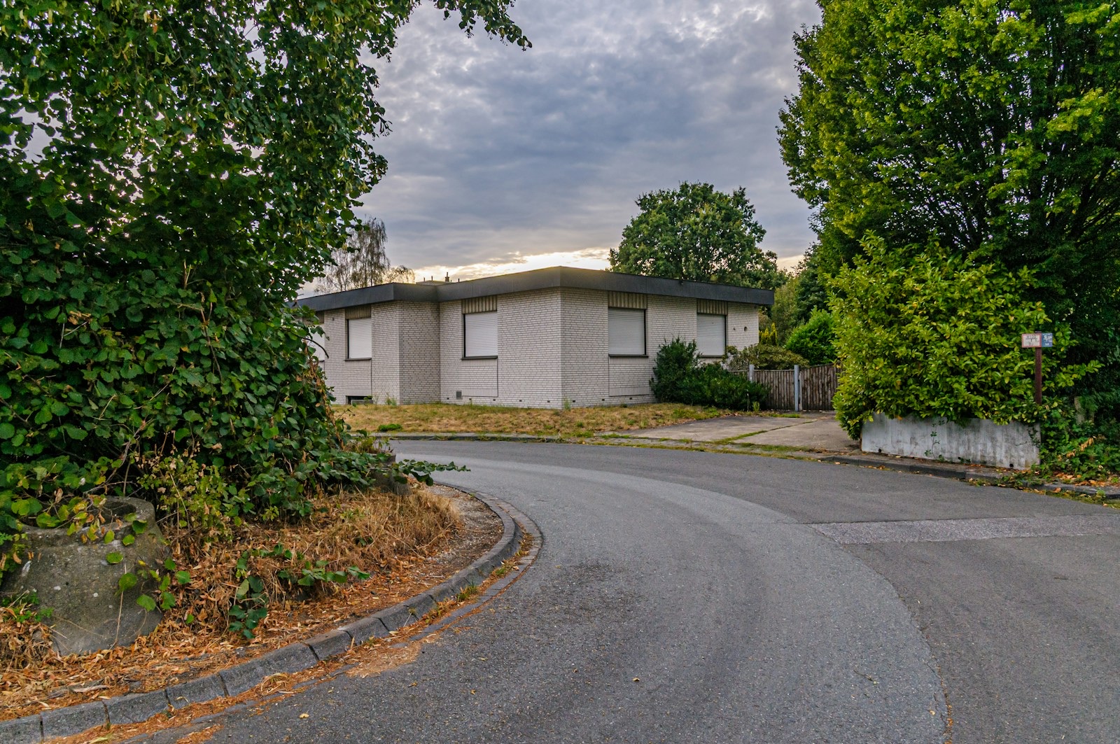 A single-story brick house with closed shutters on a quiet suburban street