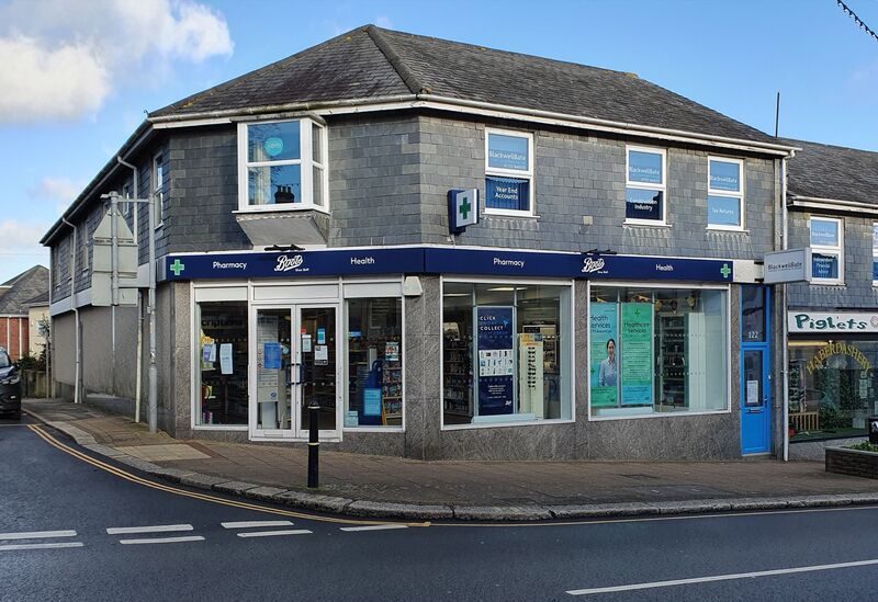 A corner shop with a dark blue Boots fascia reading Pharmacy and Health, on a street in Saltash, Cornwall.
