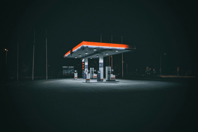 An empty petrol station with an orange-lit canopy and fuel pumps at night.