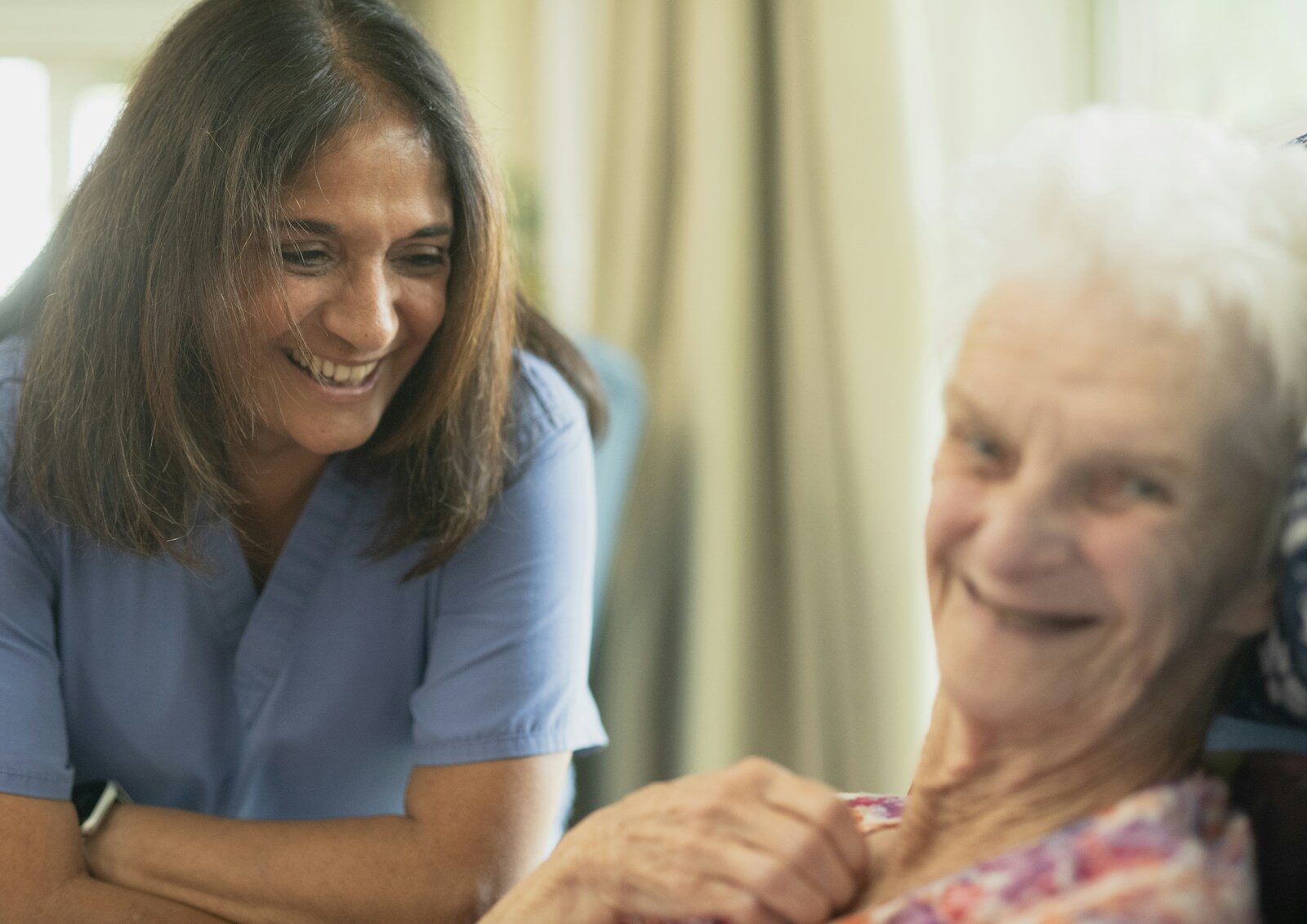 A nurse smiling with an elderly patient in a room at home