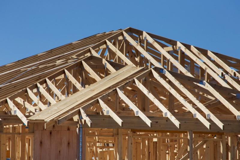 Timber wall framing and roof trusses of a new house under construction against a clear blue sky.