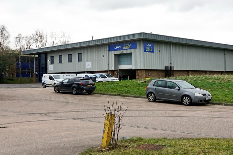 A grey single-storey warehouse with blue LKQ and Euro Car Parts signs above a loading door, white vans parked along its side and two cars in the forecourt.