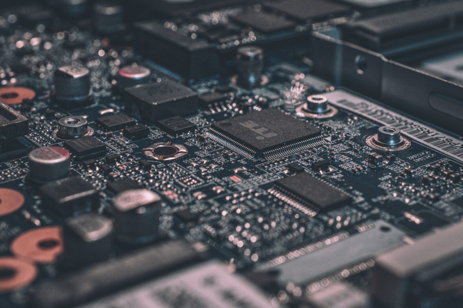 Close-up of a dark circuit board with a square microchip, capacitors and other components, in shallow focus.