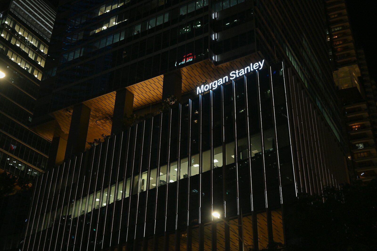 The illuminated Morgan Stanley name on the corner of a glass office tower at night.