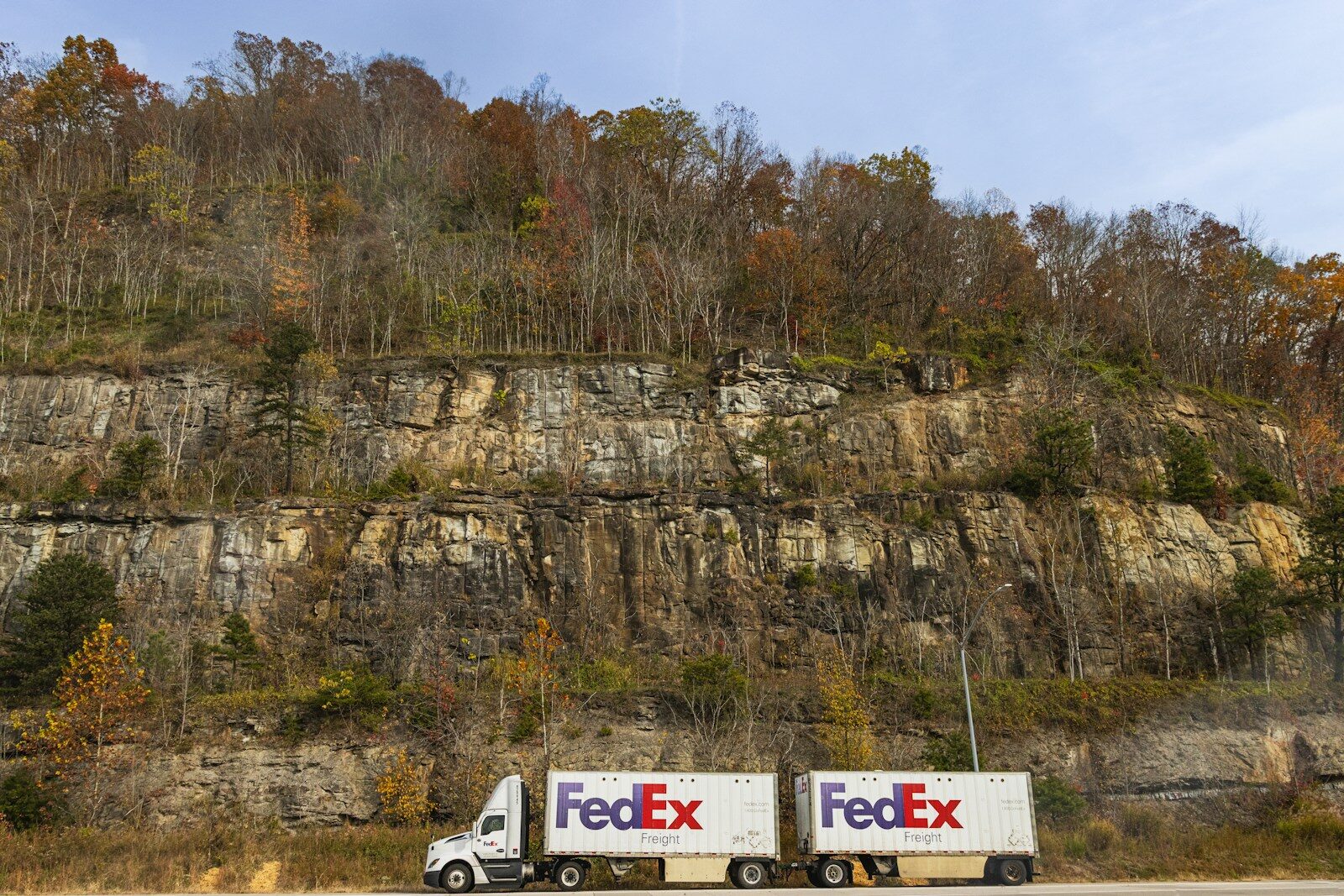 A FedEx truck driving past a rocky cliffside in autumn