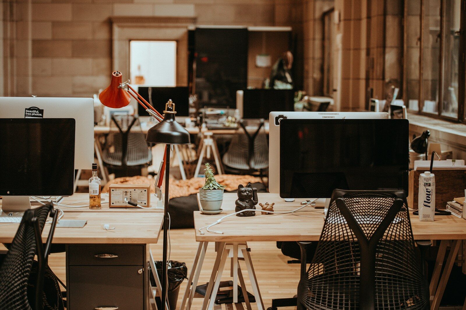 An open-plan office with unoccupied desks and dark monitor screens.