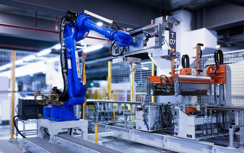 A blue industrial robot arm working alongside automated tooling on a factory production line.