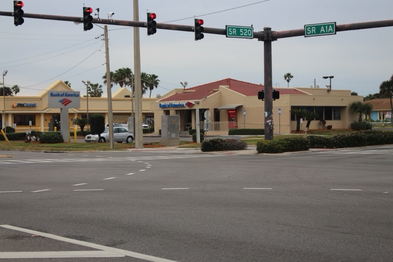 A single-storey Bank of America branch with its red, white and blue sign, seen across a road junction under traffic lights at State Road 520 and A1A.