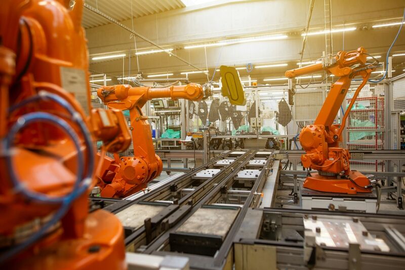 Orange industrial robot arms arranged along an automated factory assembly line