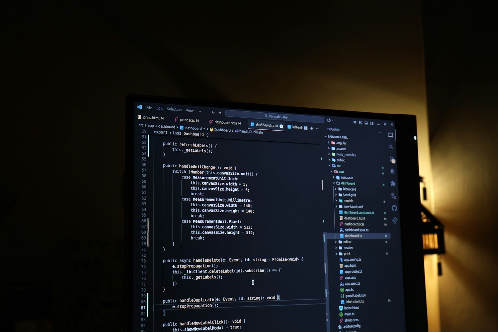 A computer monitor having source code on the screen with dark mode editor and a warm yellow light in the background