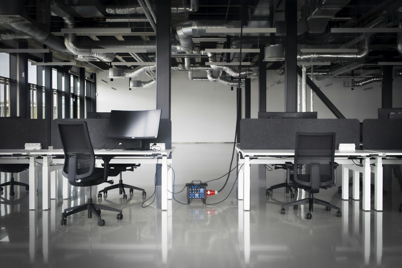 Empty modern office space under construction with installed desks and temporary power supply. An industrial workspace setting highlighting infrastructure, readiness, and contemporary office design.
