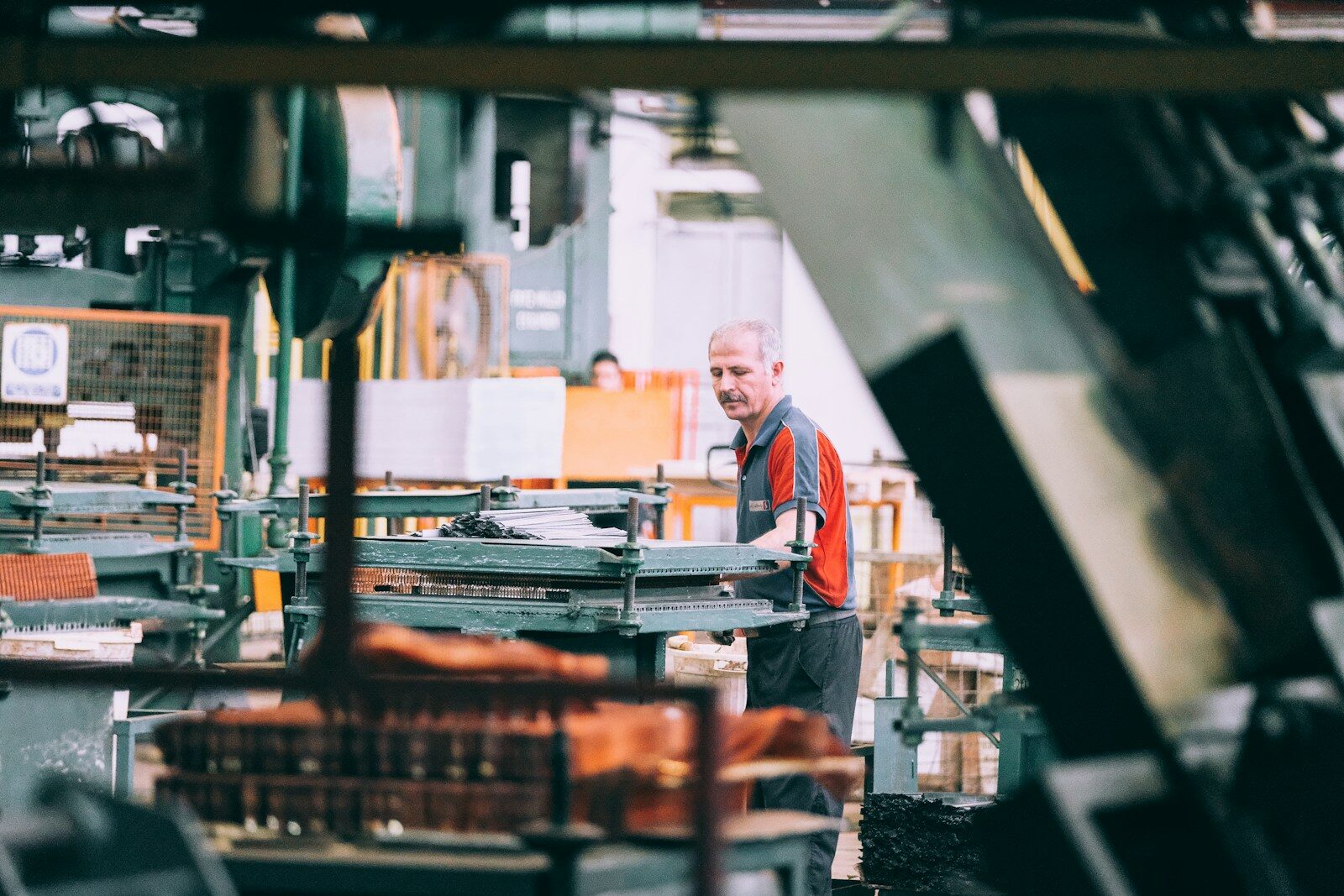 A worker in an orange polo shirt standing at a bench on a shop floor