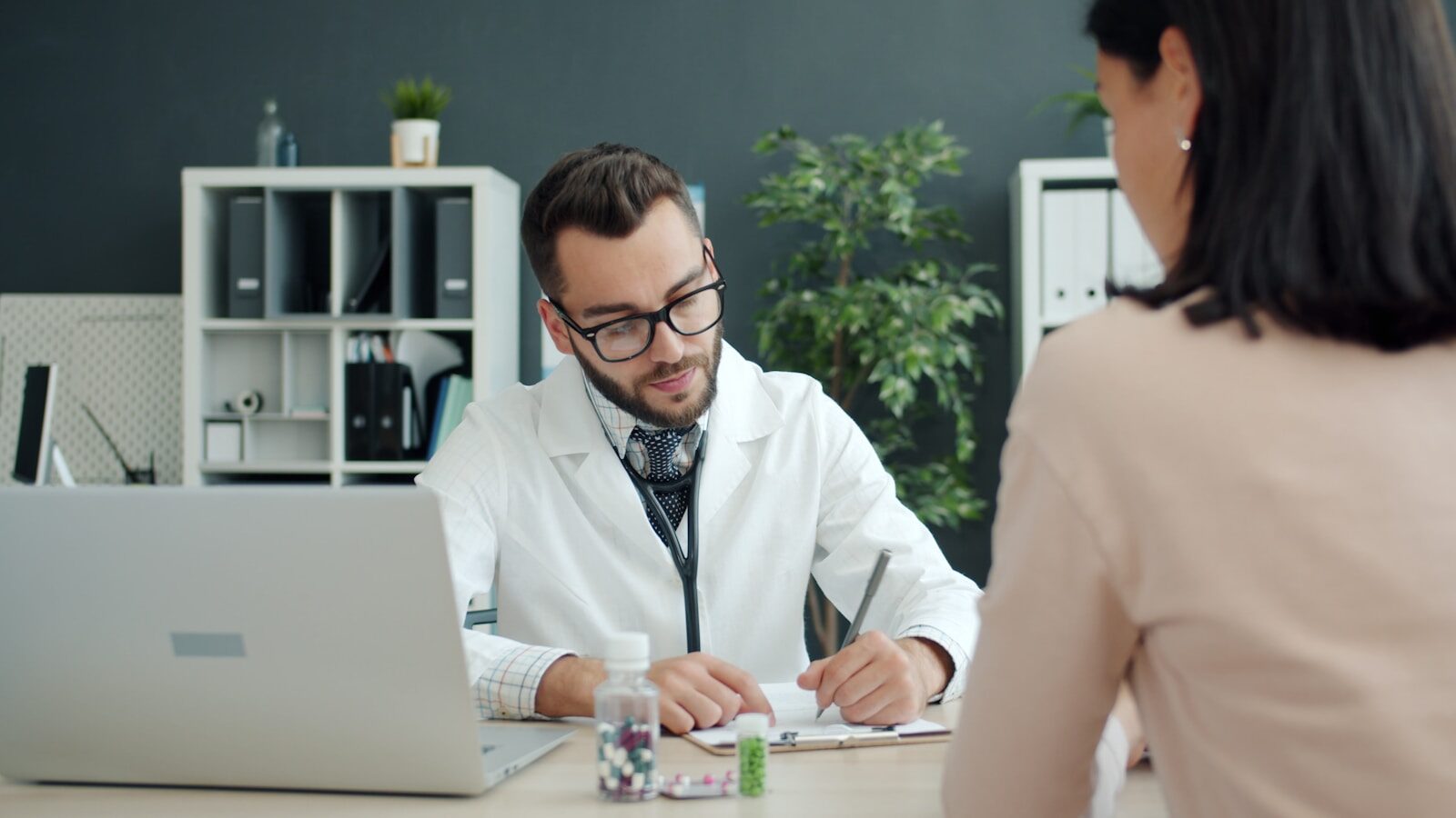 A physician taking notes while a patient sits opposite in a small practice