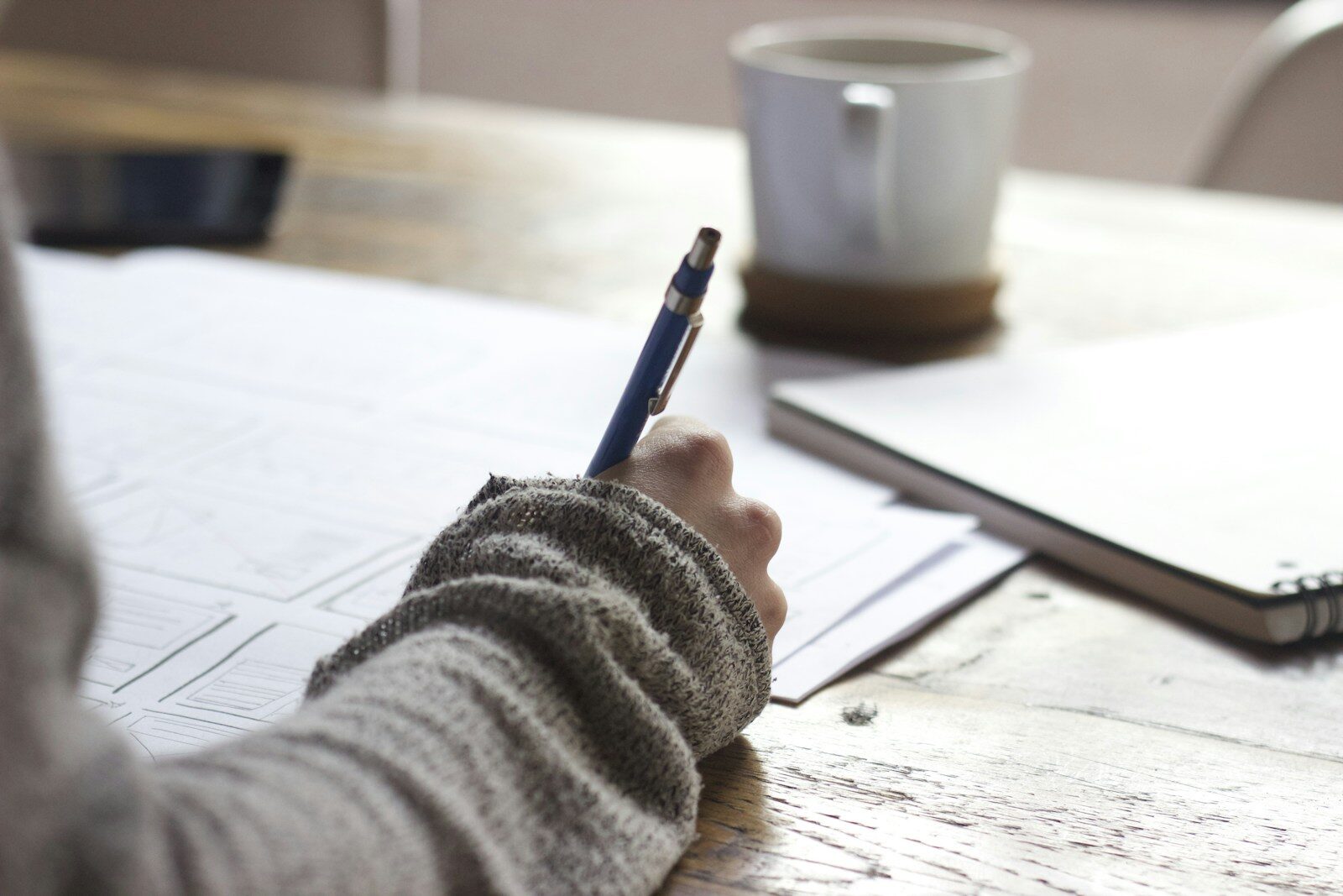 An editor marking up copy by hand at a wooden desk beside a coffee cup