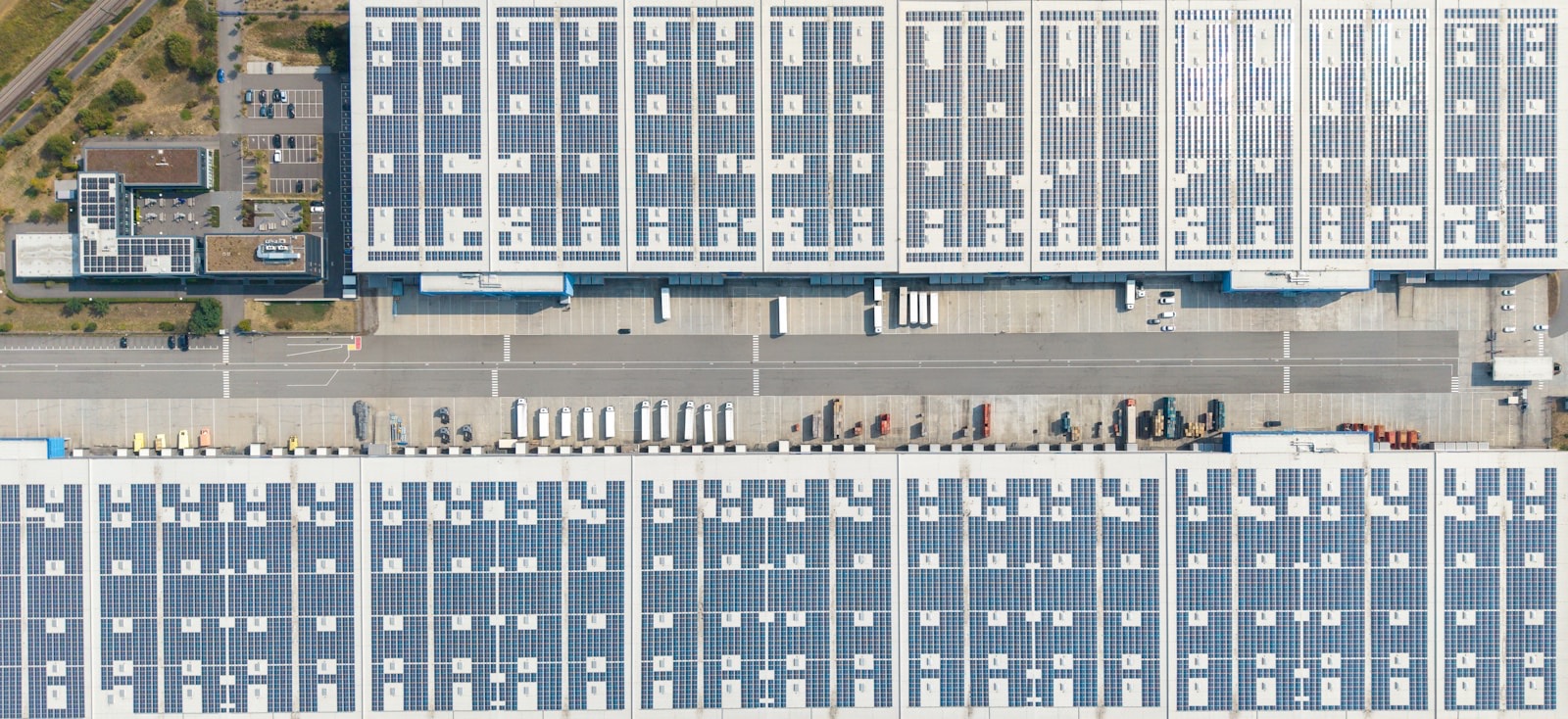 An aerial view of large warehouse roofs covered in solar panels with loading docks