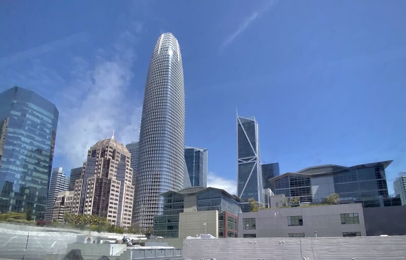 The tapered glass Salesforce Tower rising above neighbouring office buildings in downtown San Francisco under a blue sky.