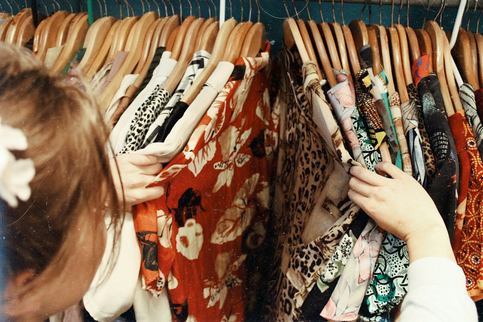 A shopper holding several garments on wooden hangers at a resale rail