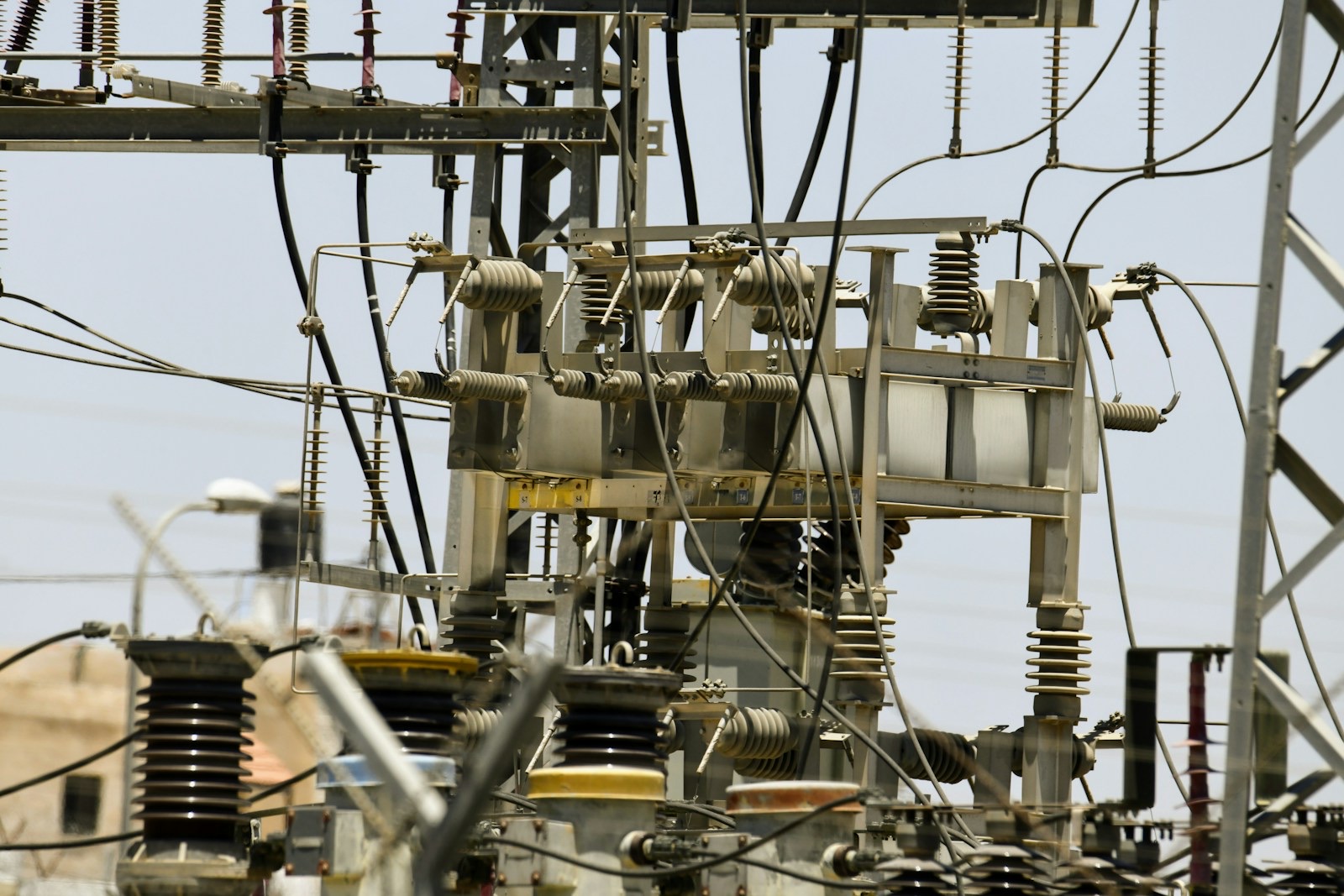 Insulators, switchgear and overhead lines at an electric power substation under a pale sky.