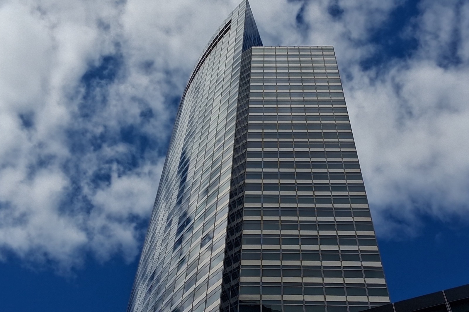The glass-and-steel tower of Goldman Sachs's headquarters at 200 West Street, seen from below against a blue sky with white clouds.