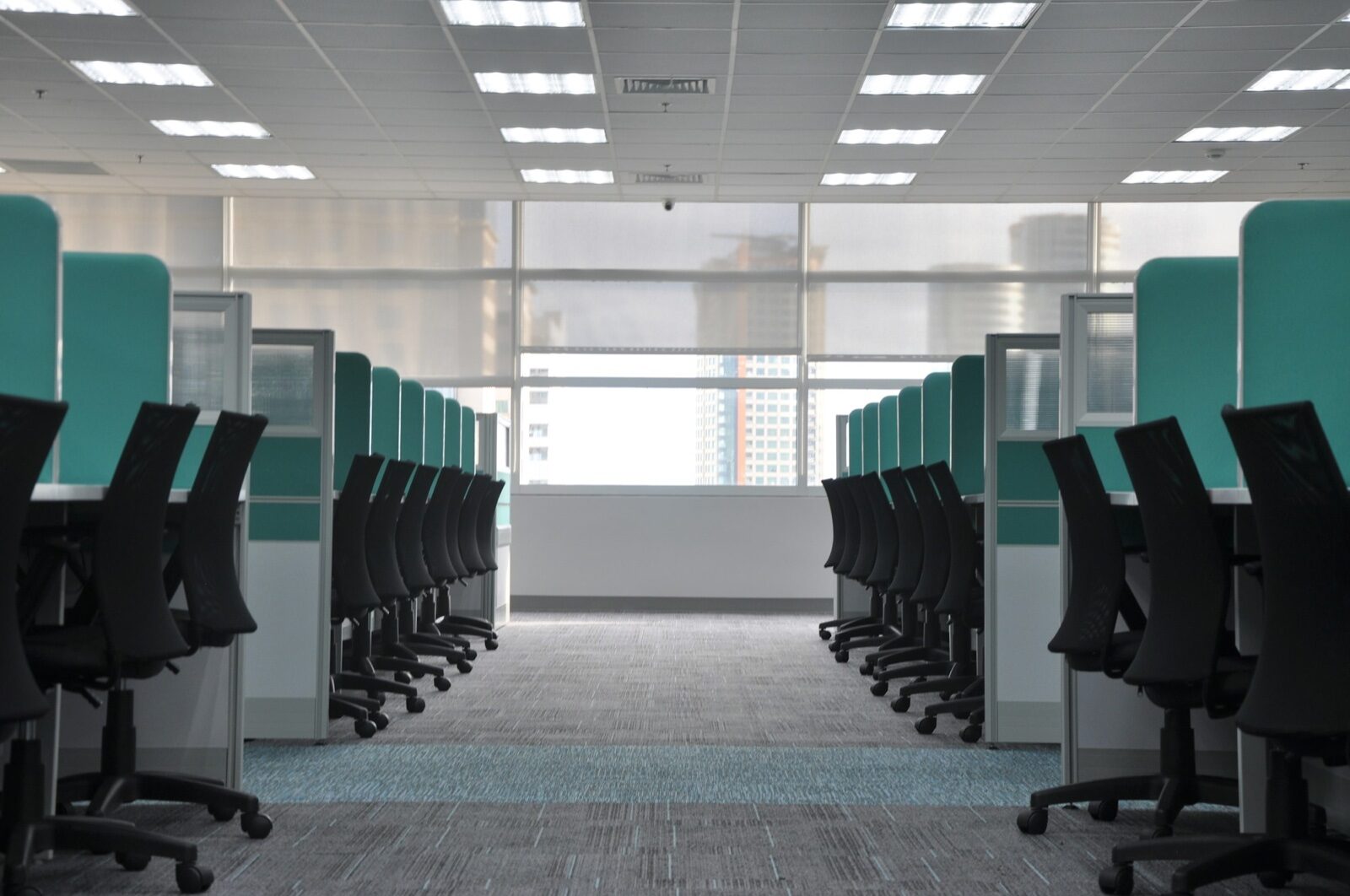 Rows of empty office cubicles with vacant chairs under fluorescent light