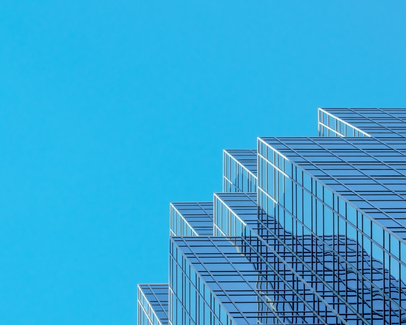 A modern glass office tower with a stepped facade rising against a clear blue sky