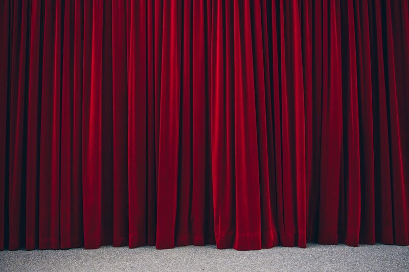A deep red pleated stage curtain, lit from the side.