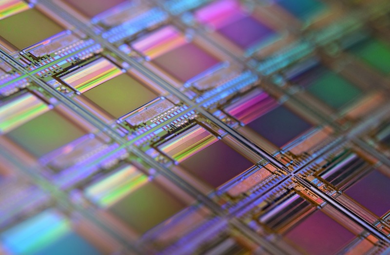 A close-up of a silicon wafer showing a grid of iridescent chip dies, in shallow focus.