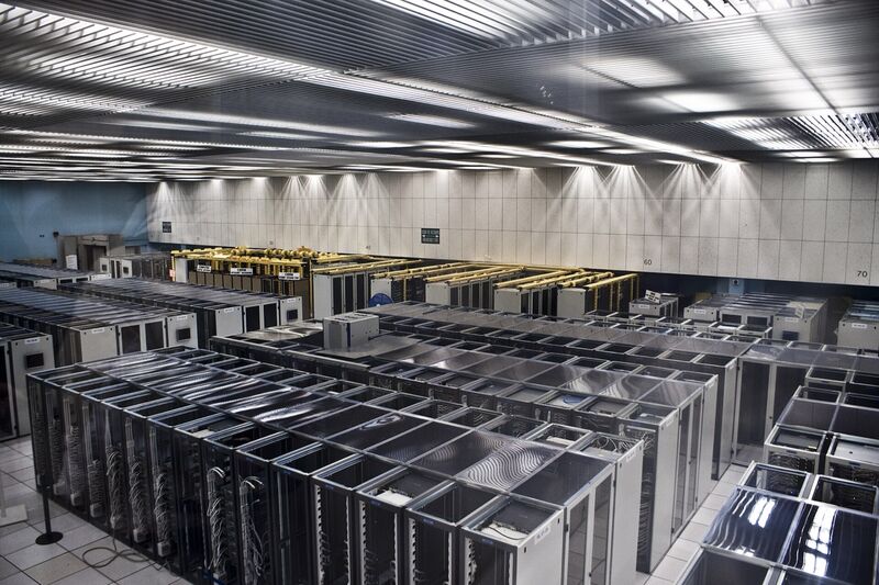 Long rows of server racks under strip lighting in a large computer hall.