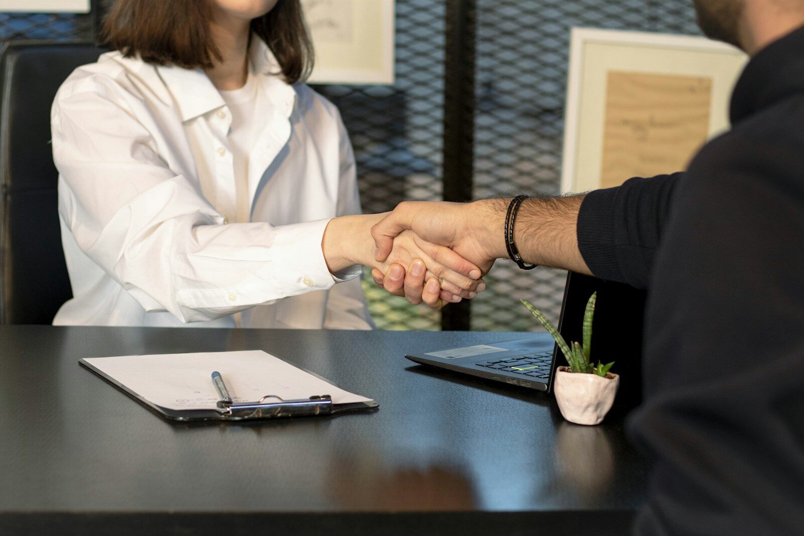 A man and a woman shaking hands across a laptop after an offer