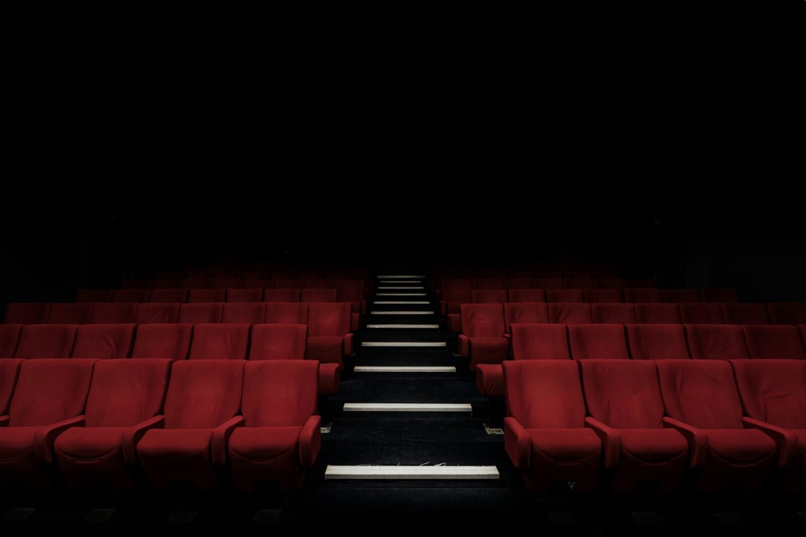 Rows of empty red seats in a darkened cinema, divided by a central aisle of lit steps.