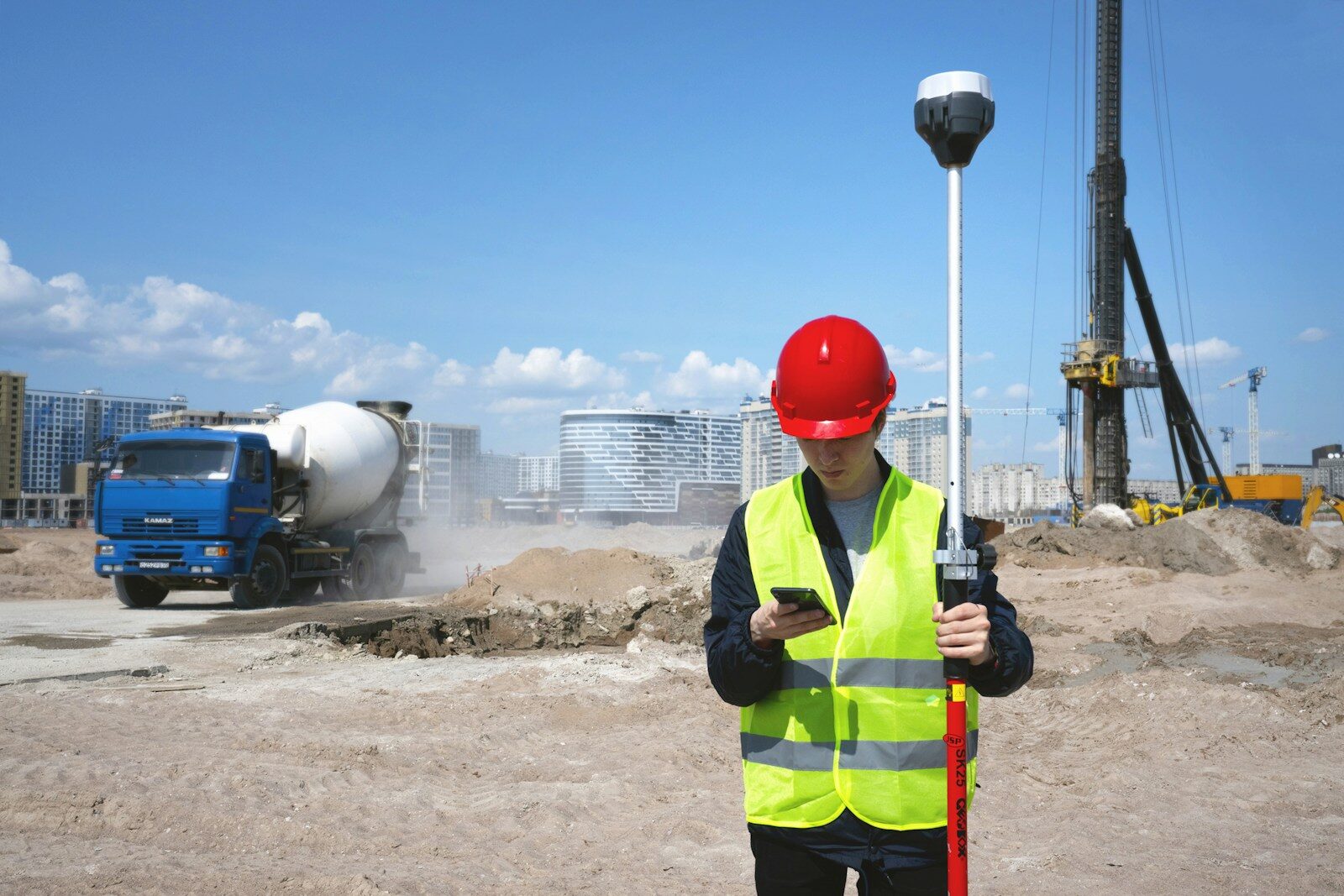 A surveyor in a hard hat and hi-vis vest on an active construction site