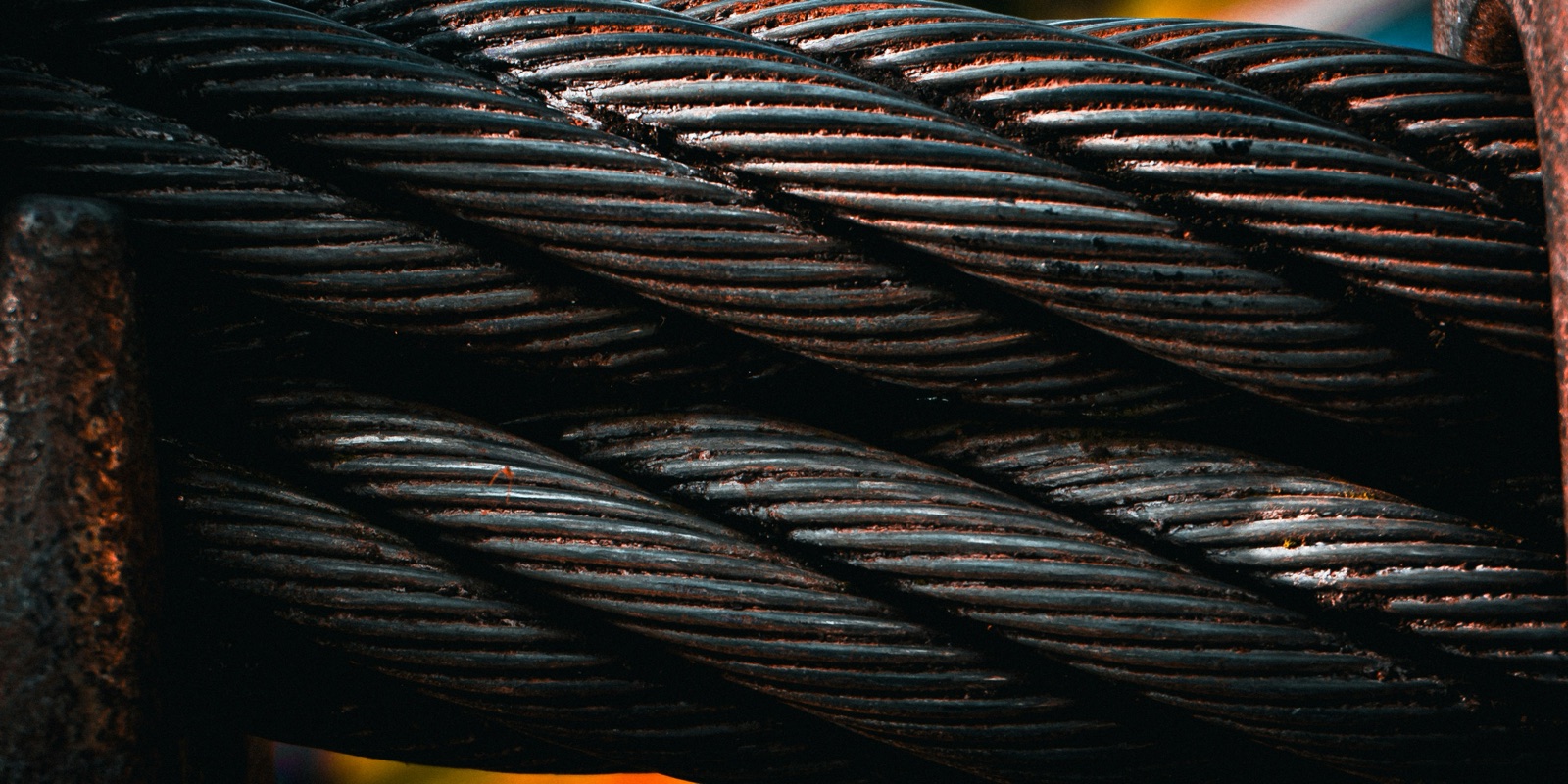 Close-up of heavy twisted steel wire rope, dark and rusted, coiled in overlapping strands.
