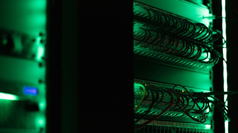 Server racks with dense cabling lit green in a dark room.
